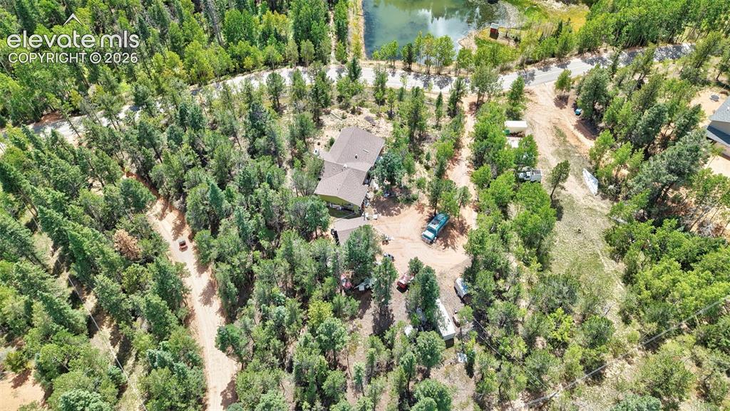 Image 3 of 21: Expansive wooded lot with a single-story residence featuring a brown shingl