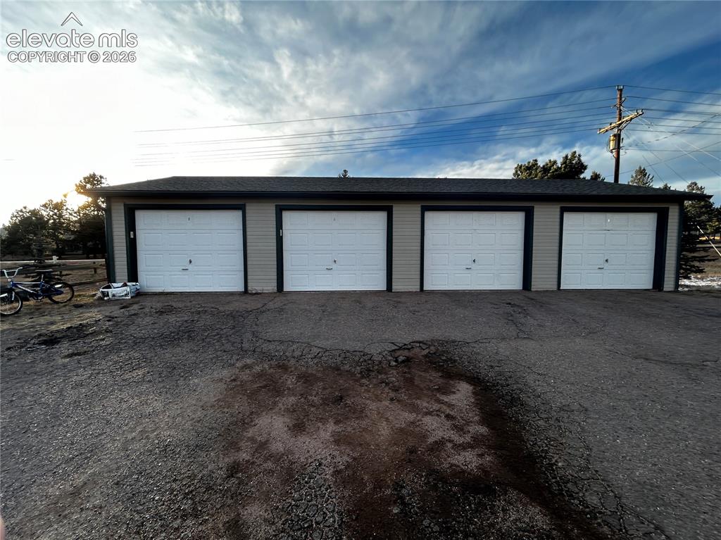 Image 12 of 12: Four-bay garage structure featuring light gray siding and white paneled gar
