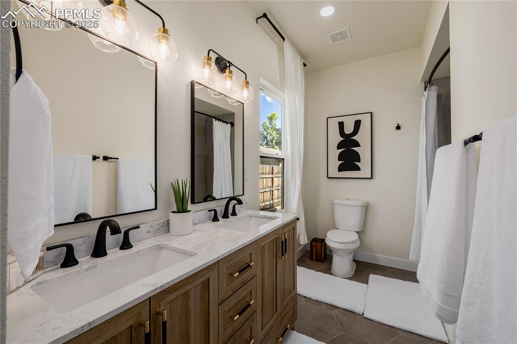 Image 23 of 39: Bathroom with double vanity, dark tile patterned flooring, recessed lightin