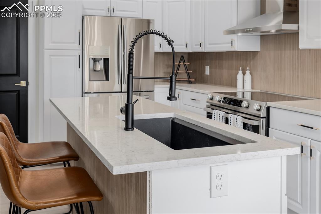 Image 8 of 39: Kitchen featuring white cabinetry, stainless steel appliances, wall chimney