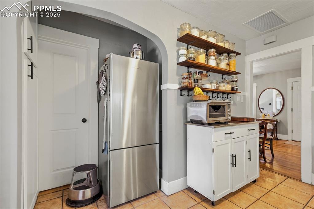 Image 16 of 49: Kitchen featuring freestanding refrigerator, white cabinetry, open shelves,