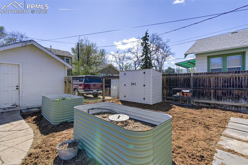 Image 36 of 49: Fenced backyard with a storage shed and a vegetable garden