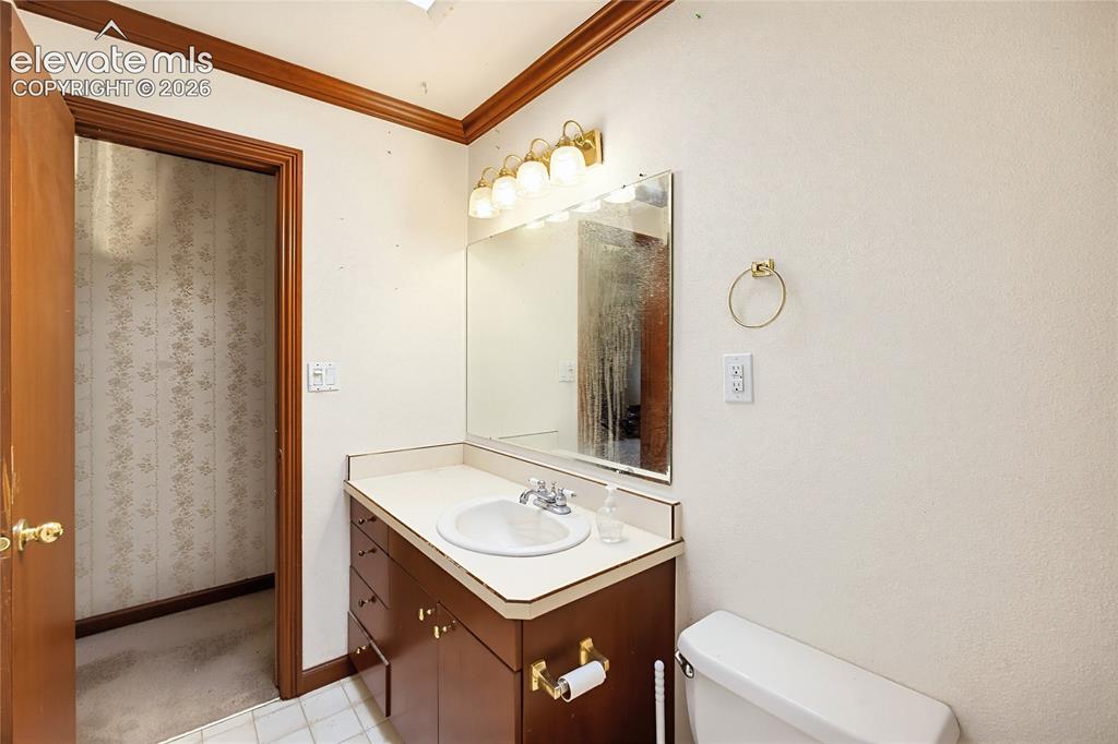 Image 12 of 45: Wood-finish vanity with an integrated basin sink, mirrored wall, and brass-