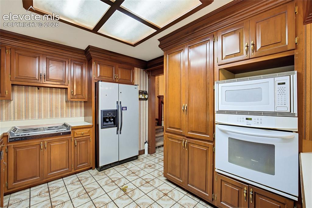 Image 24 of 45: Wood-tone cabinetry, tiled flooring, integrated wall oven, built-in microwa