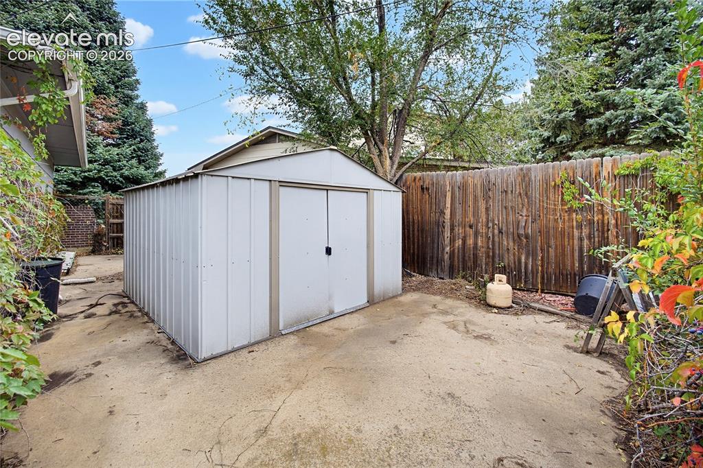 Image 5 of 45: Metal storage shed on a concrete pad, surrounded by a wood privacy fence an