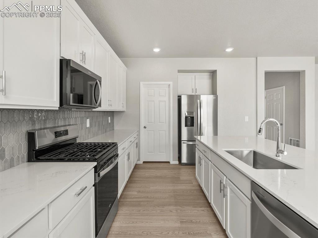 Image 4 of 26: Kitchen featuring stainless steel appliances, white cabinets, light stone c