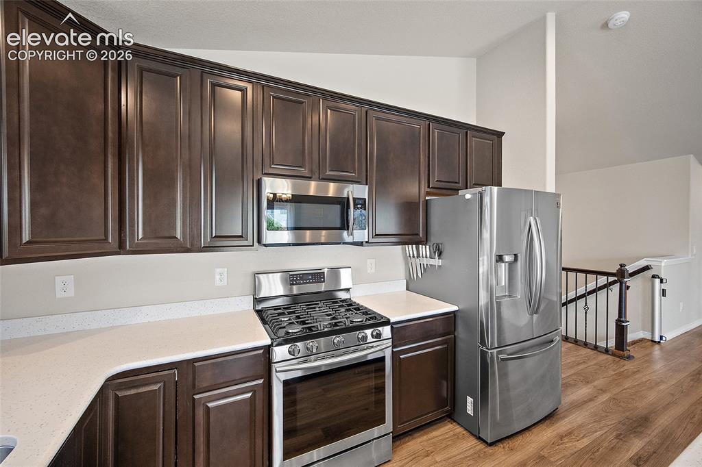 Image 10 of 49: Kitchen featuring dark wood cabinetry, light-toned countertops, stainless s