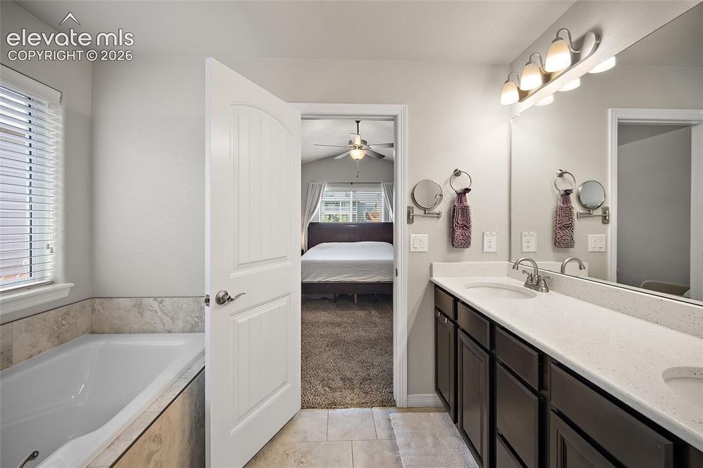 Image 17 of 49: Bathroom featuring a built-in soaking tub with stone tile surround, dual va