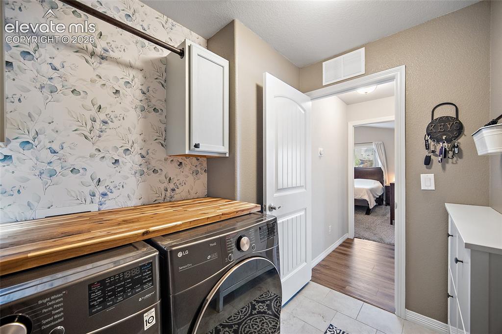 Image 19 of 49: Laundry area featuring wood-finish countertop, wall-mounted cabinetry, and