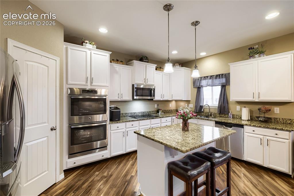 Image 4 of 32: Kitchen featuring a central island with a stone countertop, white cabinetry