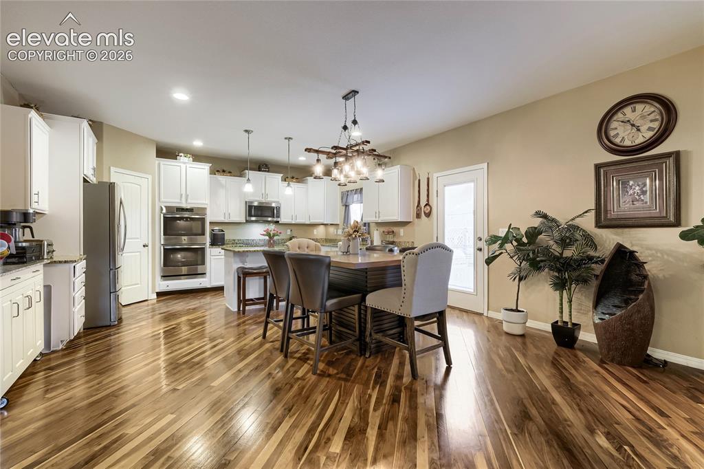 Image 6 of 32: Spacious kitchen featuring wood flooring, white cabinetry, integrated stain