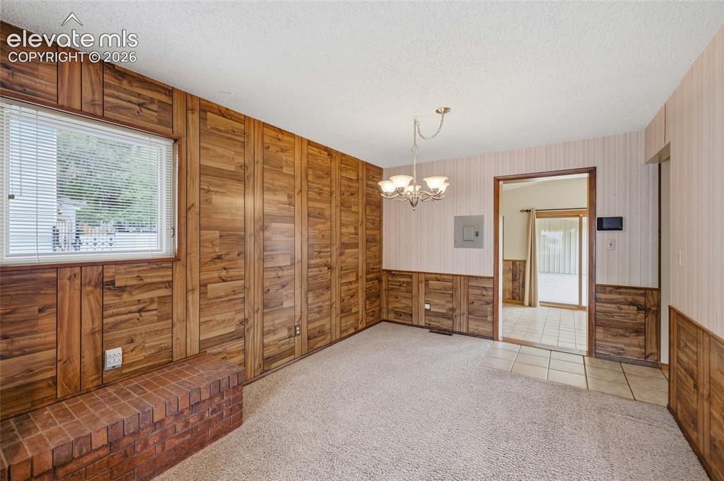 Image 10 of 43: Wood-paneled wall accents, brick hearth, window with blinds, chandelier lig