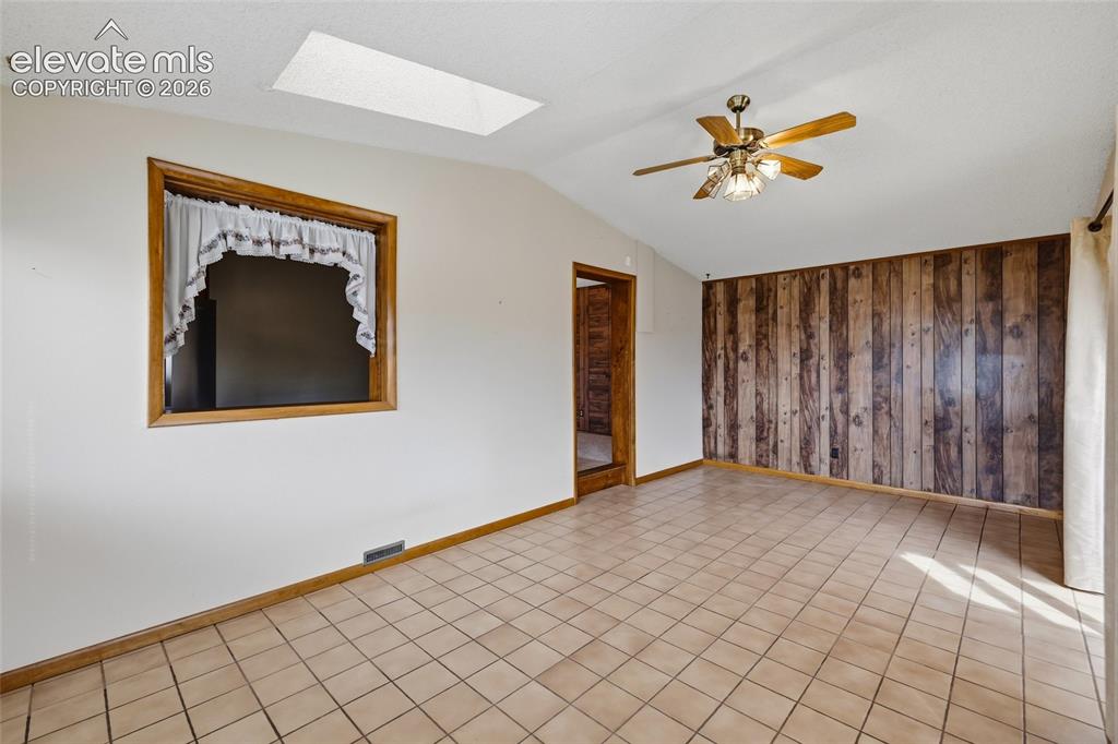 Image 15 of 43: Tiled flooring, wood panel accent wall, ceiling fan, vaulted ceiling, and r