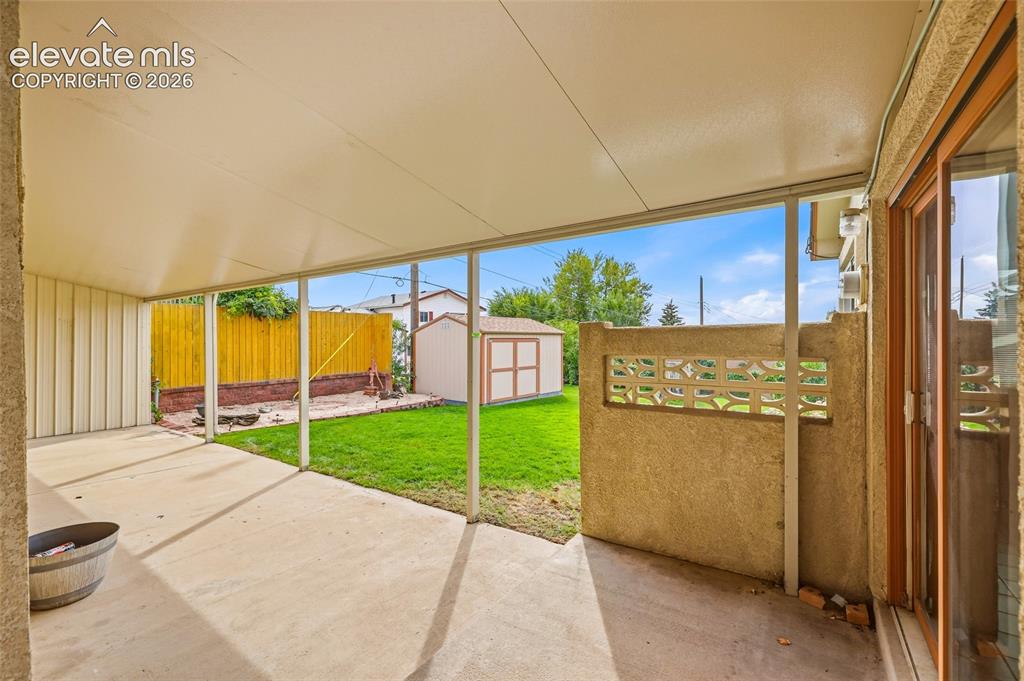 Image 26 of 43: Covered concrete patio with direct access to a grassy yard, featuring a she