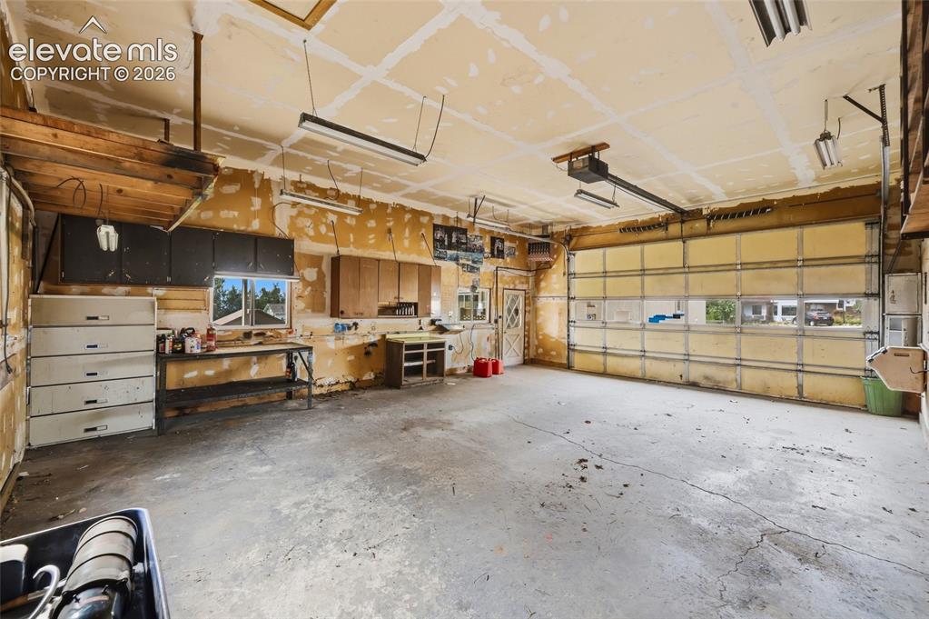 Image 29 of 43: Spacious garage with exposed ceiling joists, concrete flooring, and a large