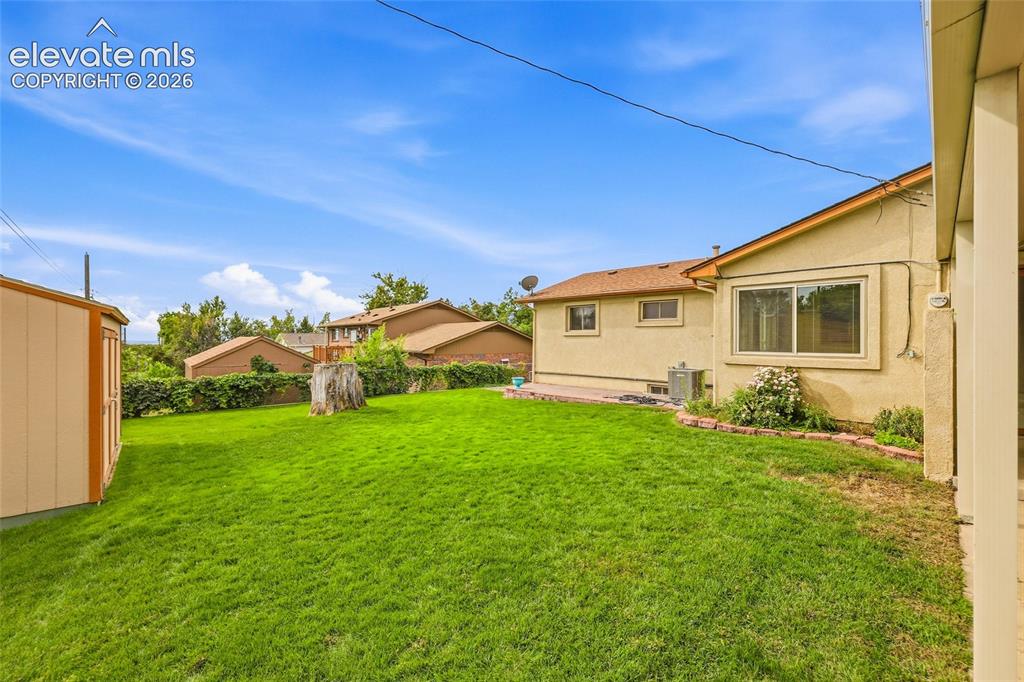 Image 30 of 43: Expansive green yard with a storage shed, stucco exterior, and a concrete p