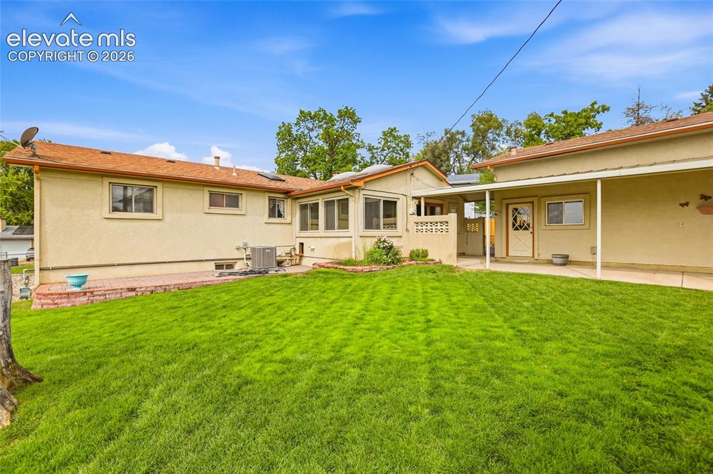 Image 31 of 43: Expansive grass lawn with a covered patio and an extended sunroom