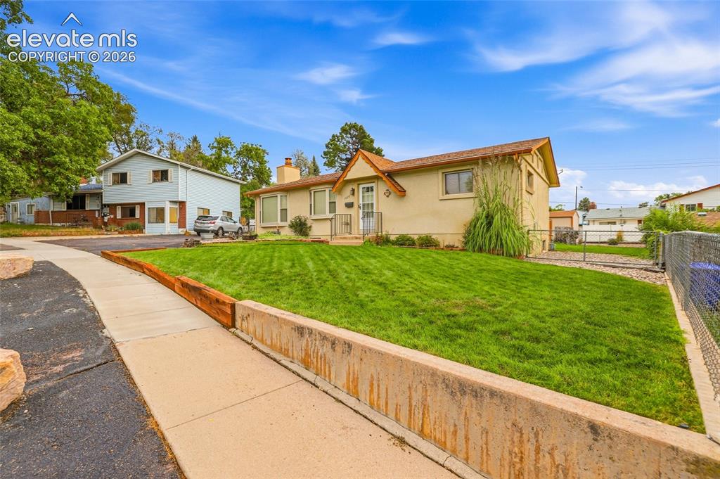 Image 39 of 43: Stucco exterior with a peaked roofline, front lawn with mature landscaping,