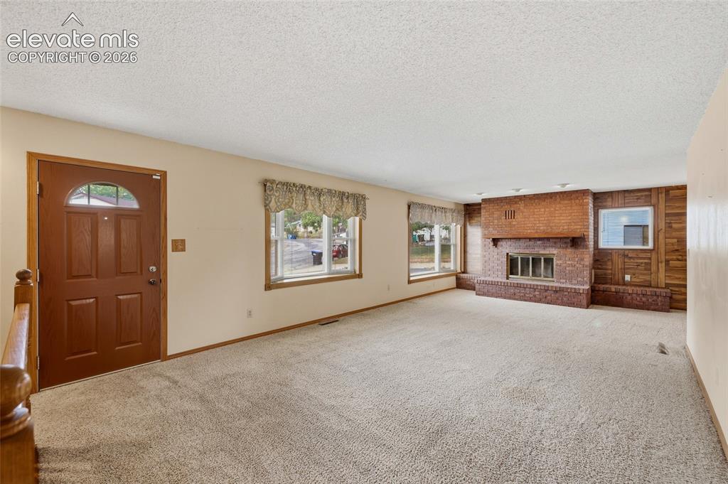 Image 7 of 43: Spacious living area featuring a brick-clad fireplace, light-colored carpet