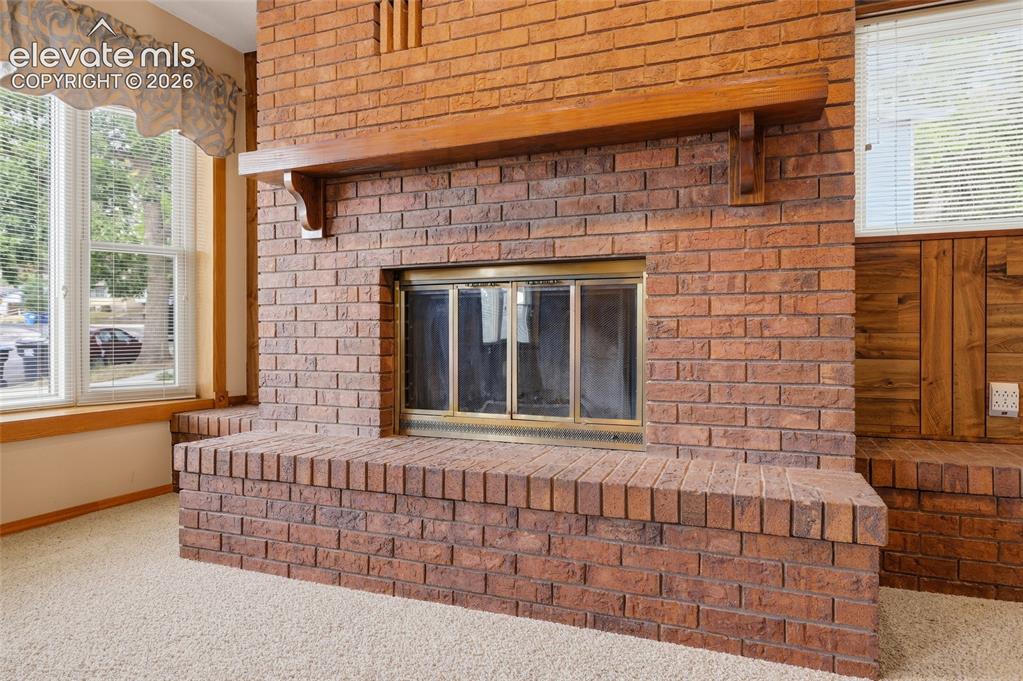 Image 8 of 43: Brick fireplace with a brass firebox, a substantial wood mantel, and an ele