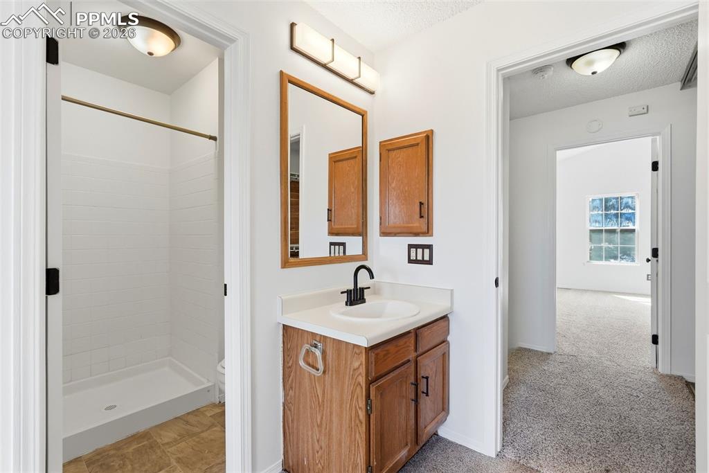 Image 25 of 44: Full bath with vanity, a stall shower, light carpet, and a textured ceiling