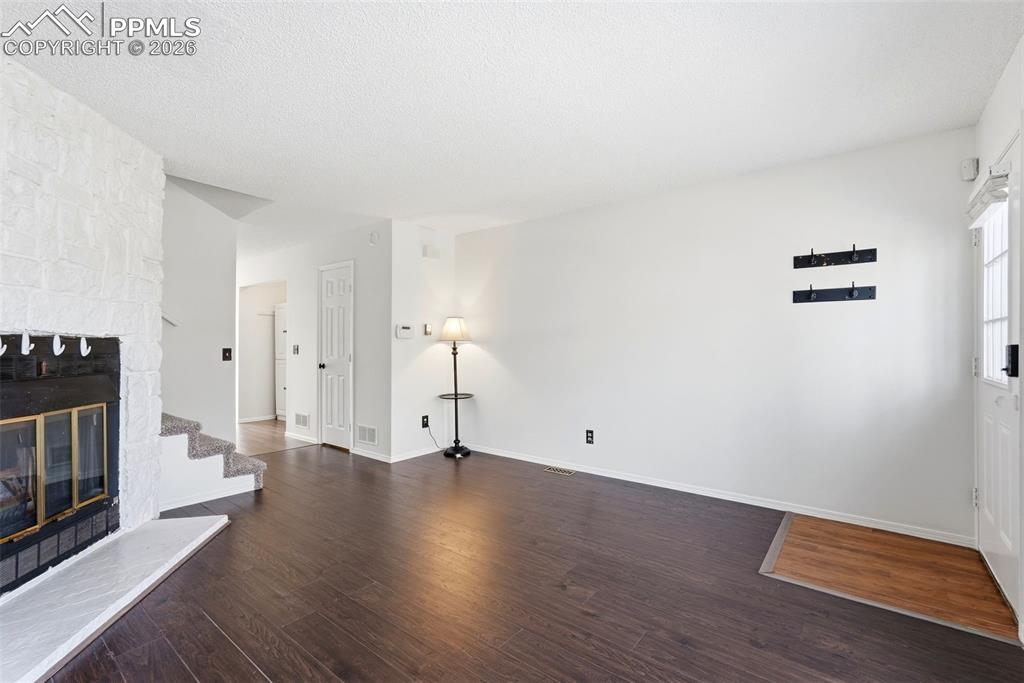 Image 7 of 44: Unfurnished living room featuring dark wood-type flooring, a stone fireplac