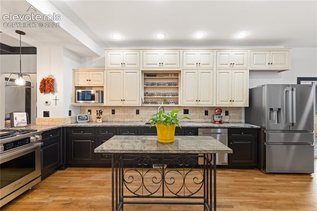 Image 22 of 45: Spacious kitchen featuring wood-finish flooring, two-tone cabinetry, stone 