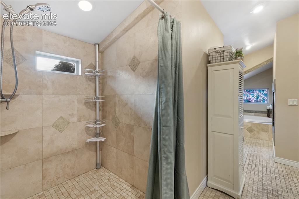 Image 32 of 45: Tiled shower with handheld showerhead, corner shelf, and small rectangular 