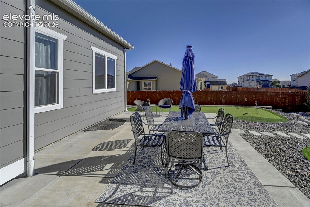 Image 10 of 48: Expansive concrete patio with a decorative area rug, leading to a putting g