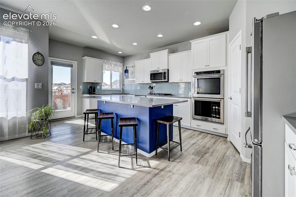 Image 12 of 48: Kitchen featuring a blue island with seating, white cabinetry, built-in sta