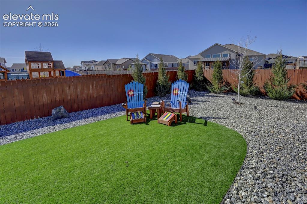 Image 4 of 48: Expansive backyard featuring a manicured artificial turf lawn, a gravel bor