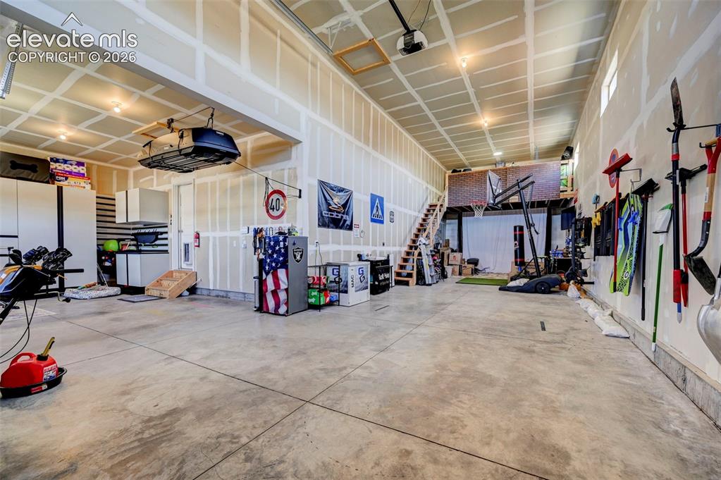 Image 48 of 48: Spacious garage with high ceilings, exposed joists, and concrete flooring