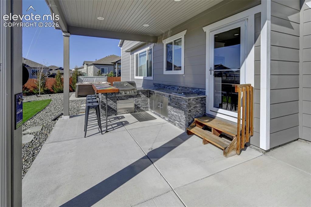 Image 7 of 48: Covered concrete patio with built-in outdoor kitchen, integrated grill, and