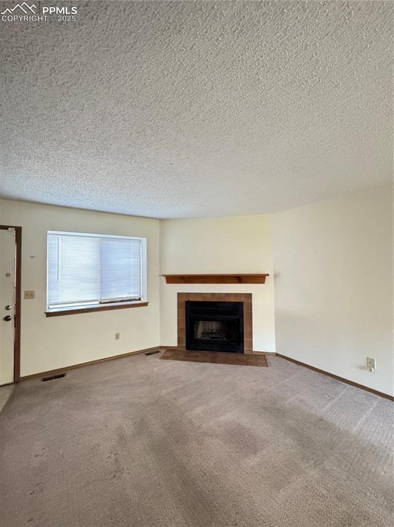 Image 2 of 11: Unfurnished living room with a textured ceiling, a tile fireplace, and carp