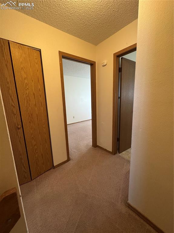 Image 7 of 11: Corridor featuring a textured ceiling, light colored carpet, and a textured