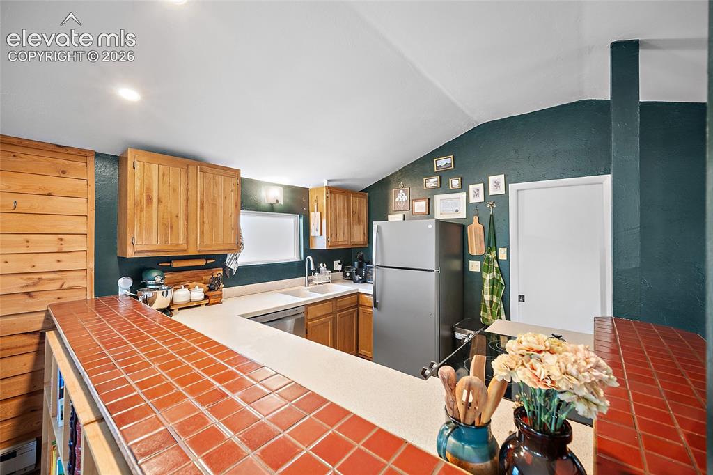 Image 10 of 31: Cozy kitchen showcasing rich red tile countertops, knotty-pine walls, and s
