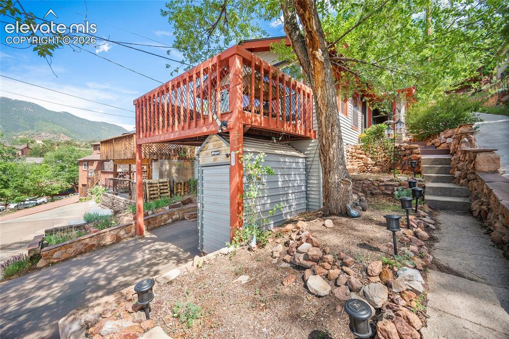 Image 28 of 31: Unique hillside property featuring an elevated red deck, covered carport wi