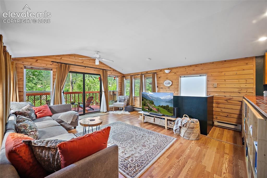 Image 5 of 31: Bright open-concept living room with warm knotty-pine accent walls, vaulted