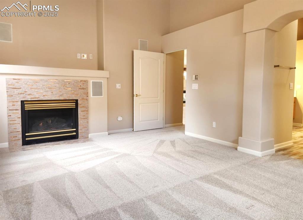 Image 10 of 34: Unfurnished living room featuring a high ceiling, carpet floors, arched wal