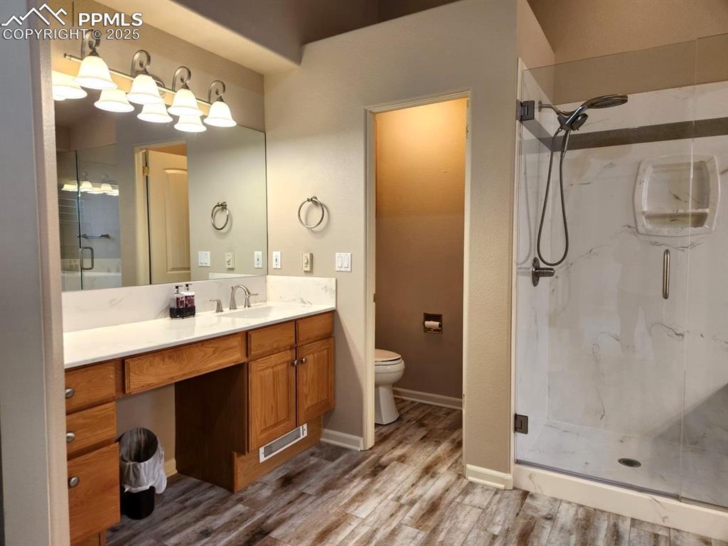 Image 14 of 34: Bathroom with a marble finish shower, wood finished floors, and vanity