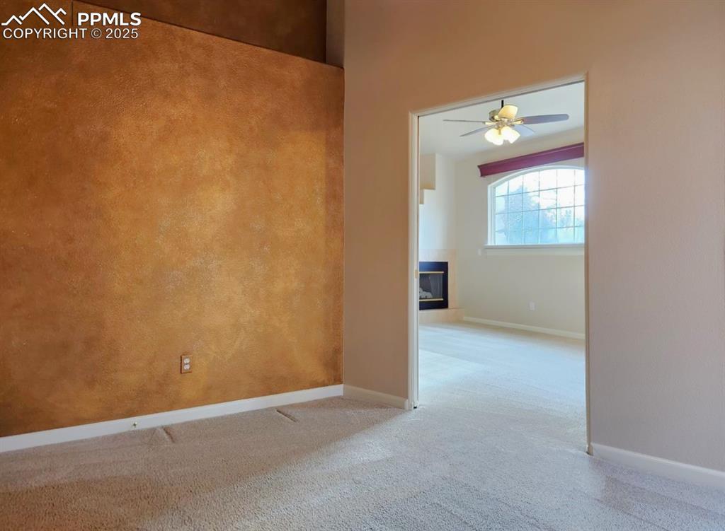 Image 21 of 34: Empty room with carpet flooring, a ceiling fan, and a glass covered firepla