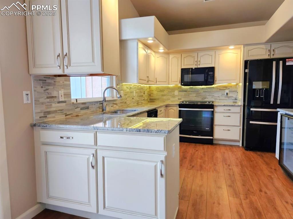 Image 4 of 34: Kitchen featuring black appliances, light stone countertops, a peninsula, l