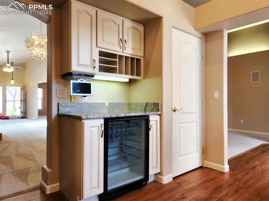 Image 5 of 34: Kitchen featuring beverage cooler, light stone counters, dark wood-style fl