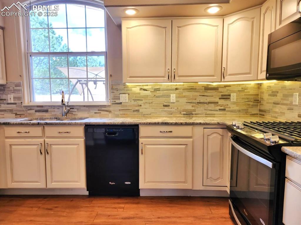 Image 6 of 34: Kitchen with black appliances, white cabinets, and tasteful backsplash