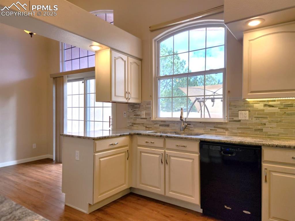 Image 7 of 34: Kitchen featuring black dishwasher, light wood-style floors, decorative bac