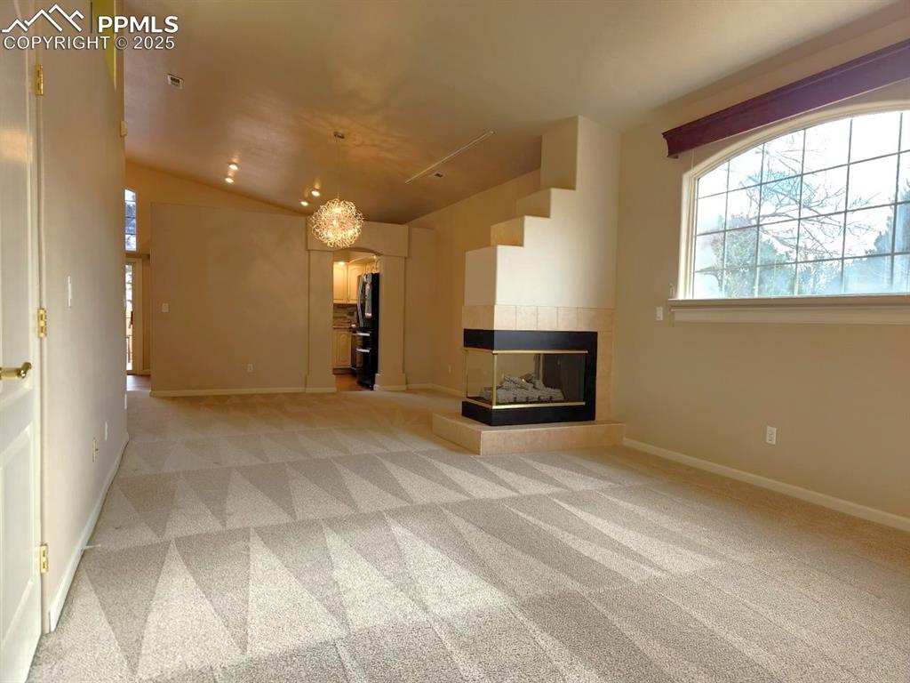 Image 9 of 34: Unfurnished living room with arched walkways, light carpet, a tiled firepla