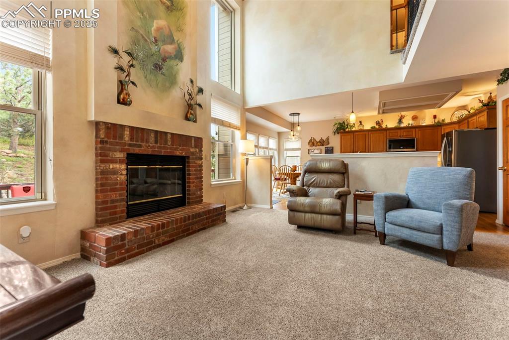 Image 12 of 50: Living room with a high ceiling, a brick fireplace, and light colored carpe