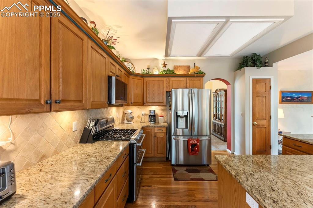 Image 17 of 50: Kitchen featuring decorative backsplash, stainless steel appliances, arched