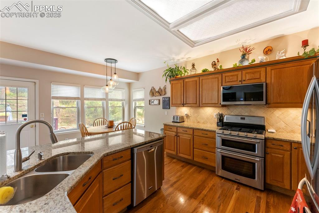 Image 18 of 50: Kitchen featuring light stone counters, stainless steel appliances, brown c