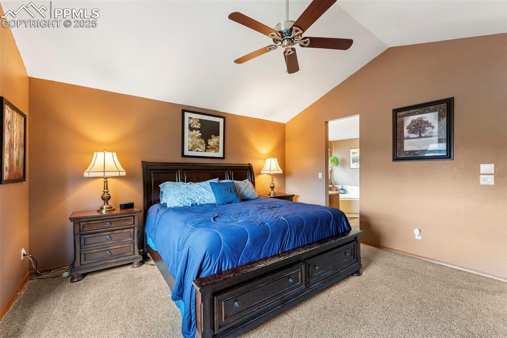 Image 26 of 50: Carpeted bedroom with lofted ceiling, ensuite bath, and ceiling fan
